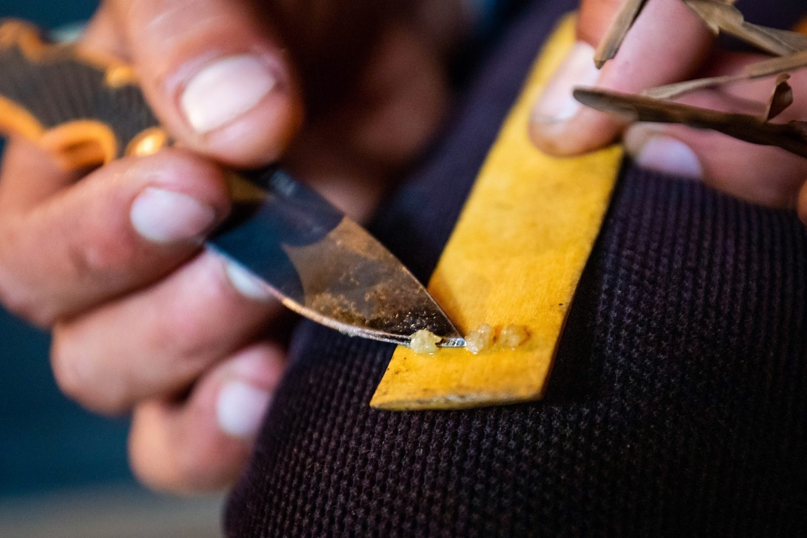 Close-up of hands holding a bamboo stick with Kambo medicine, as a practitioner carefully scrapes the Kambo resin with a knife to prepare for the ceremony.