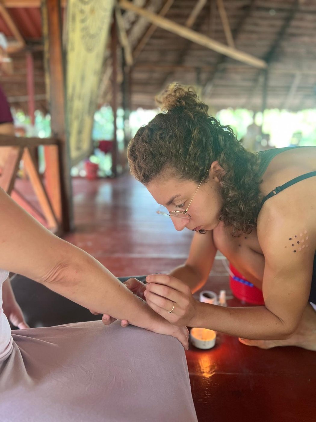 Kambo practitioner using an incense stick to carefully burn small "gates" onto a participant's arm in preparation for applying Kambo medicine during a traditional ceremony.